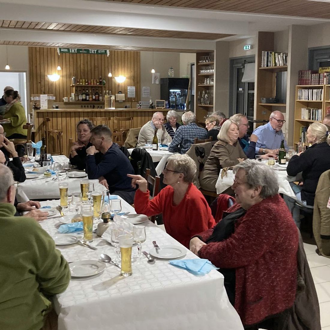 La salle du Chat Qui Pêche un soir de repas : tables dressées, une trentaine de personnes attablées, le comptoir en bois au fond